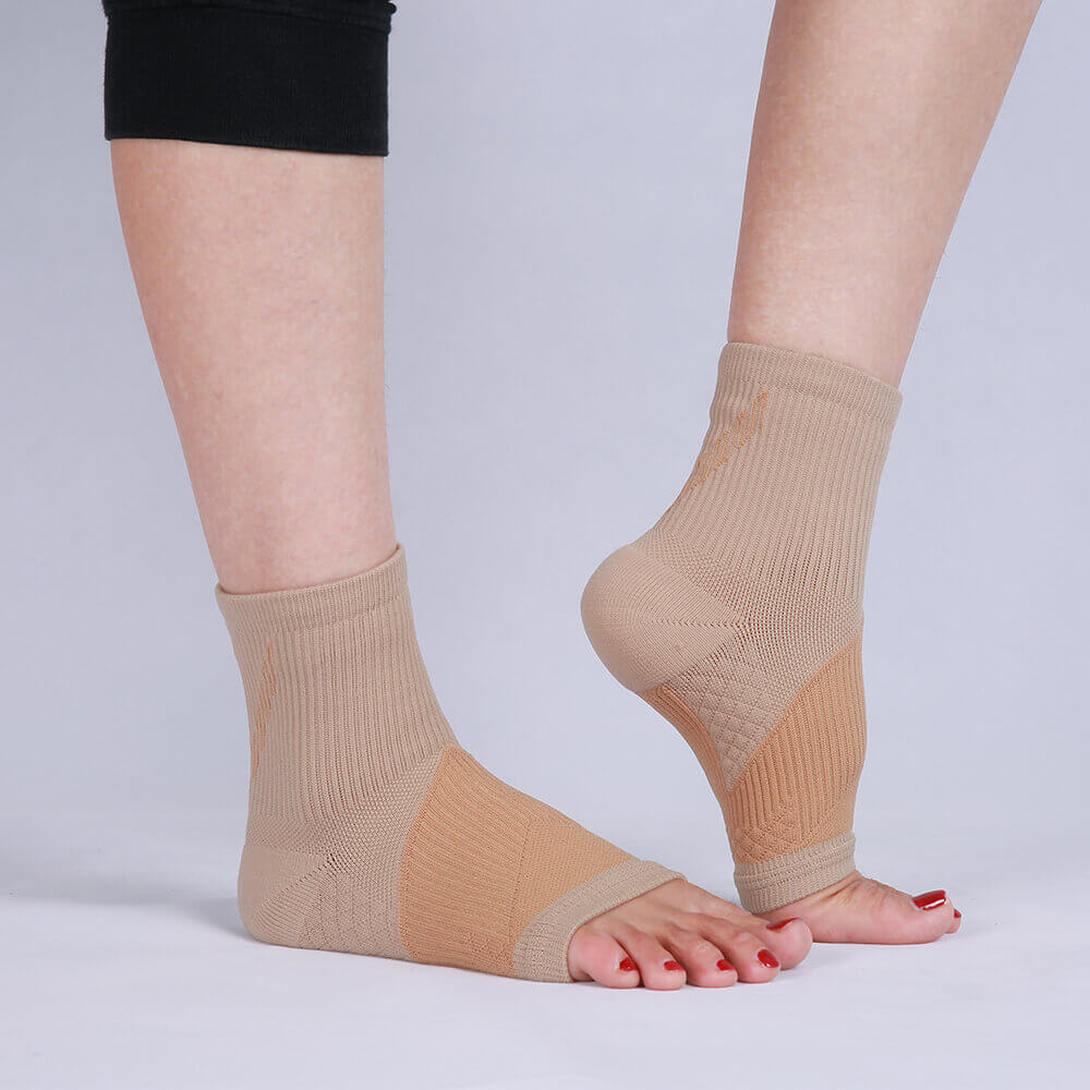 Ankle compression sleeves in beige on a person's feet, aiding support.