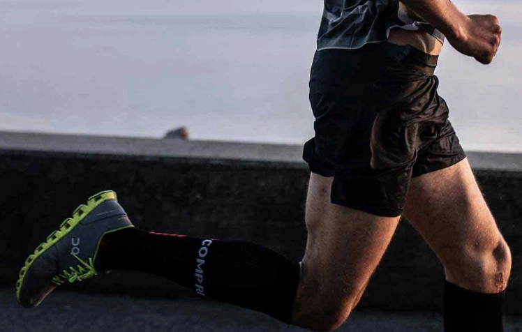A runner wearing black compression socks and running shoes.