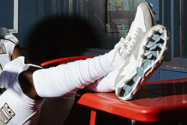 A football player rests on a red table, showing off their white scrunch socks and cleats