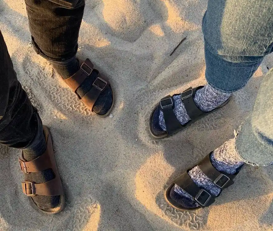 Socks and sandals on the beach: Four feet in various socks and sandals on sandy ground.