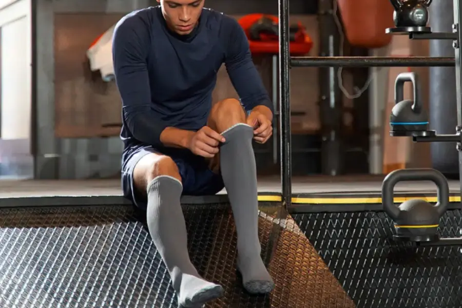 A man prepares to wear deadlift socks in a gym, adjusting them on his calves.