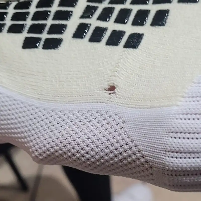 Grip socks bottom close-up showing small hole defect in knit beneath black grip pads