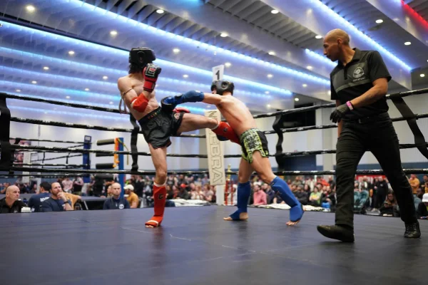 muay thai fighters competing in a ring, one delivering a kick while wearing padded shin socks