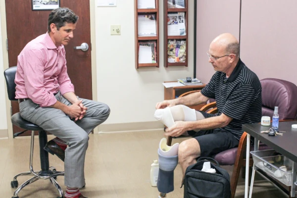 Prosthetist talks with patient wearing stump socks and trying on a prosthetic leg.