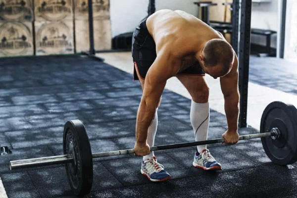 Deadlift socks protect shins of a man grabbing a barbell in a gym.