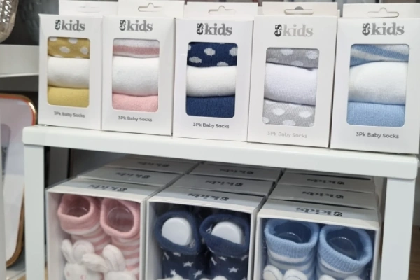 Infant socks display on shelves in a store, packaged in various colors and patterns.