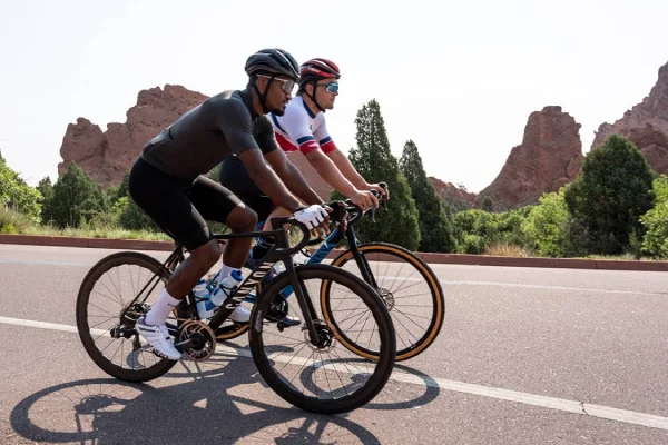 Two male cyclists, wearing road cycling socks, ride on a scenic road.