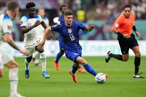 A professional soccer player wearing shin guard socks dribbles the ball during a game.