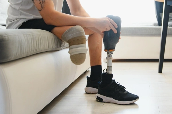 Amputee sitting on a couch, adjusting a prosthetic with prosthetic socks on.