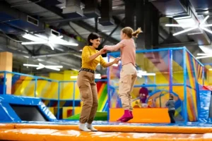 A mom and her child wearing trampoline grip socks jump together in an indoor park.