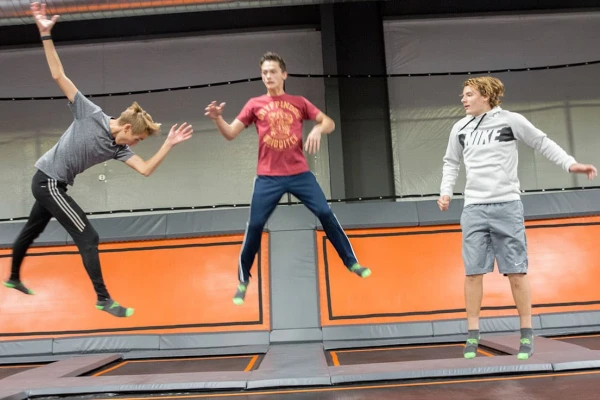 Young male friends jumping on trampolines in a trampoline park, wearing grip socks.
