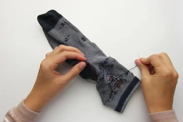 Hand repairing a sock hole with darning needle and thread