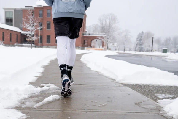 Runner’s legs in winter running socks on a snowy path, highlighting gear choice for cold conditions