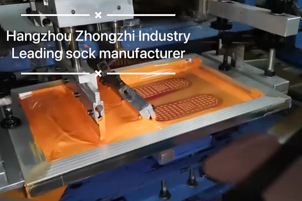 An automated machine applying an orange design to socks using the screen printing method