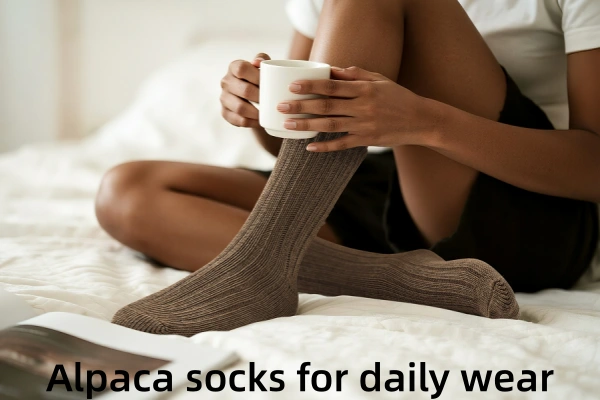 A woman wearing comfortable brown alpaca wool socks and holding a mug while sitting on a bed.
