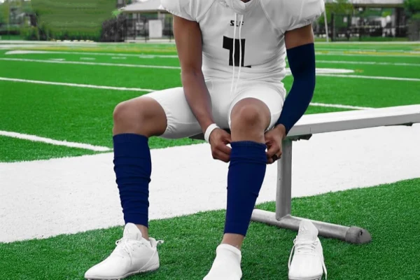 Football player wearing blue football leg sleeves socks and arm sleeves on a bench.