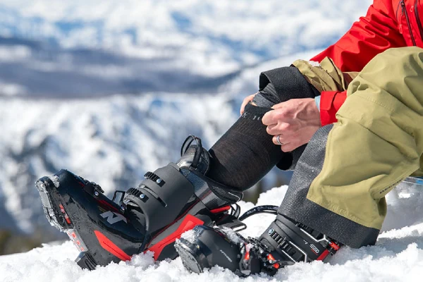 A skier puts on black skiing socks while sitting in the snow.