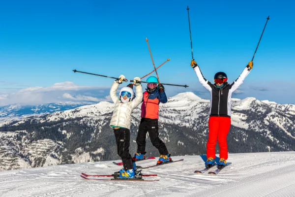 Three friends celebrating their successful skiing adventure on a sunny mountaintop.