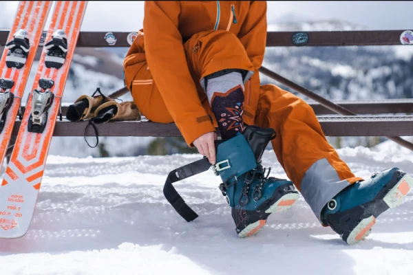 A snowboarder adjusts their snowboard socks and boots on a snowy mountain.
