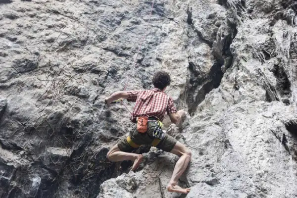 Climber barefoot in traditional climbing shoes on rock, focusing on sensitivity and feel