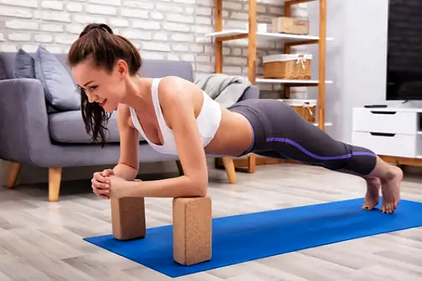 Woman demonstrating forearm plank variation using two wooden Yoga Blocks for support and stability on a blue mat