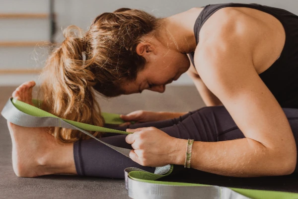 Woman using a Yoga Strap (Belt) to deepen a seated forward bend stretch