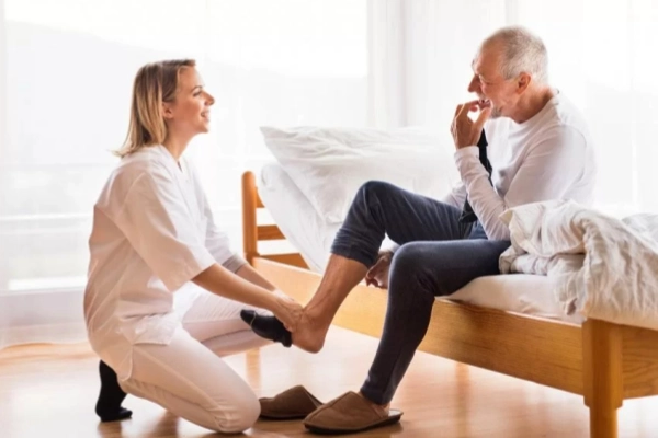 Caregiver assisting an older man with foot support illustrating plantar fasciitis socks for seniors