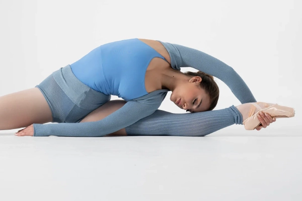 Lyrical dancer extending a leg to show a long arch line in stirrup tights under stage lighting