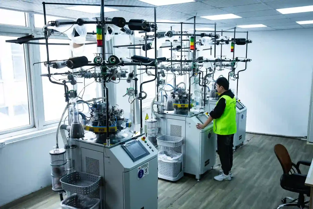 Factory worker in safety vest monitoring automated medical compression socks machine in modern manufacturing facility