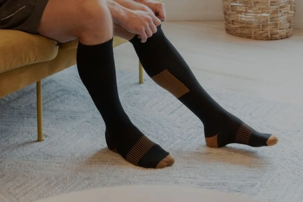 Copper compression socks being put on by a man sitting on a yellow couch