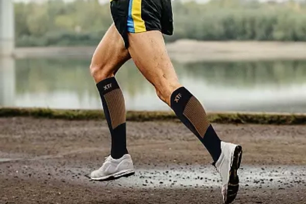 Copper compression socks worn by a male athlete running outdoors near a river