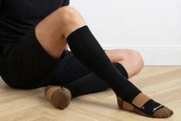 Copper compression socks worn by a man sitting on the floor in black sportswear