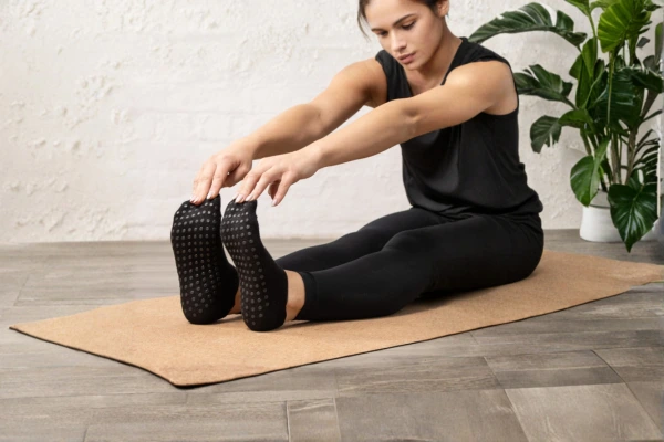 Yoga grip socks worn by a woman stretching on a cork mat indoors