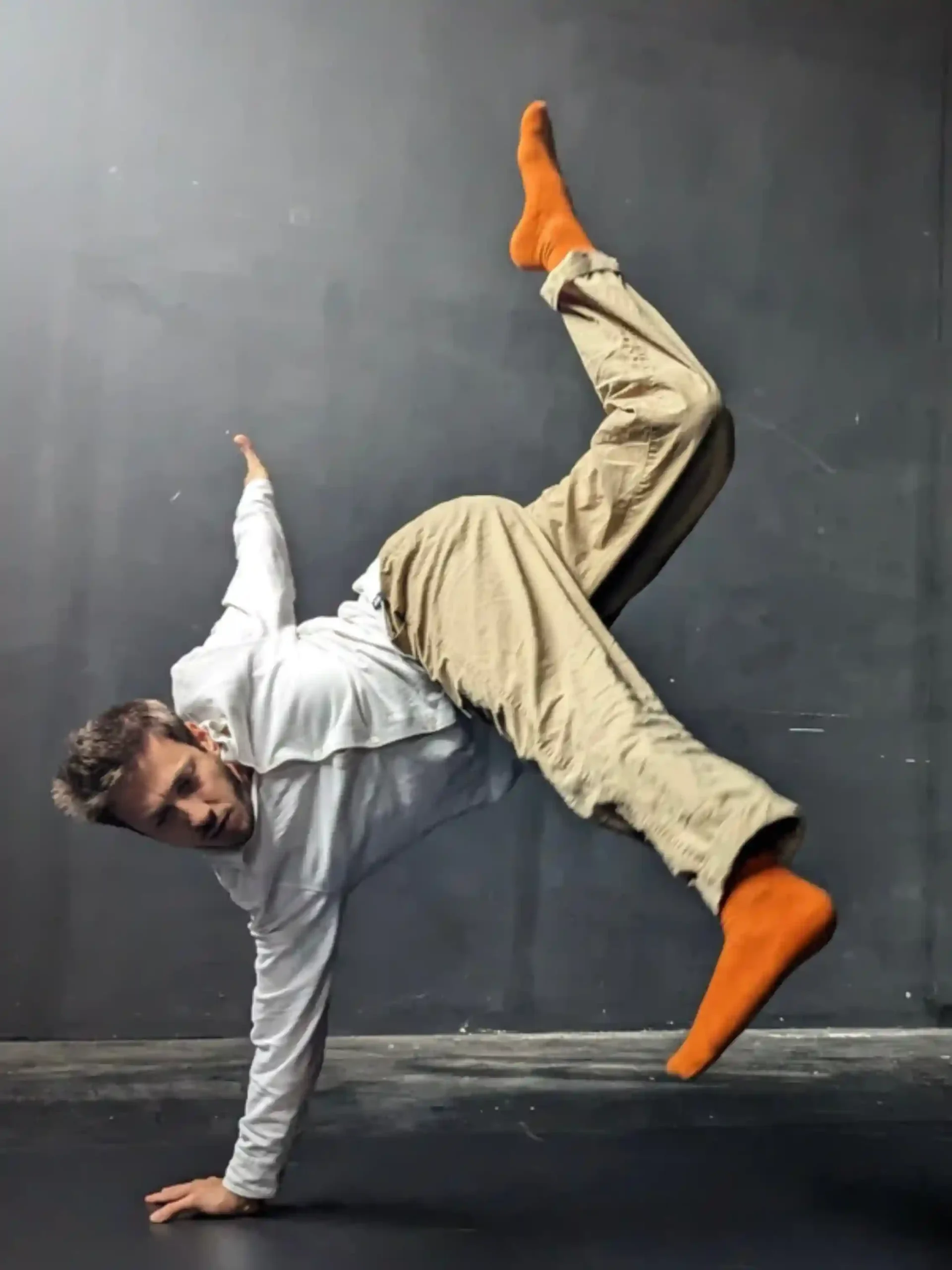 Male contemporary dancer wearing orange grip socks while performing a one-hand stand