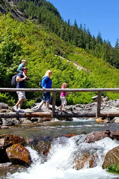 Family hiking across a mountain stream trail wearing lightweight summer hiking shoes and socks
