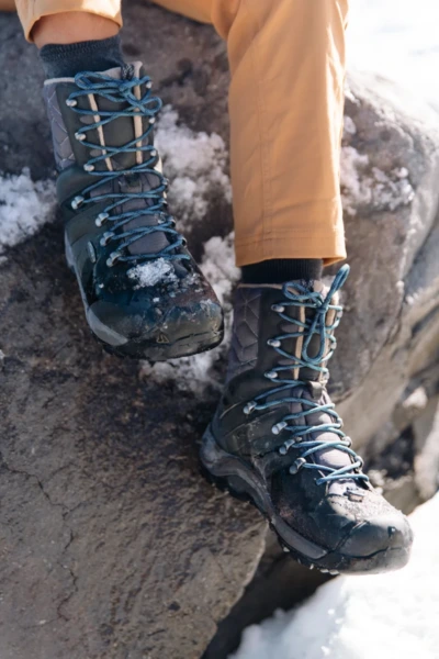 High cut backpacking boots paired with tall cushioned hiking socks on snowy rocks