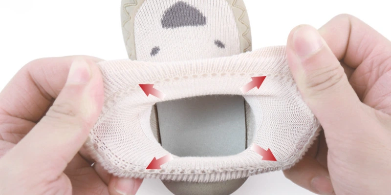 hands stretching elastic knitted upper of baby sock shoe showing wide opening