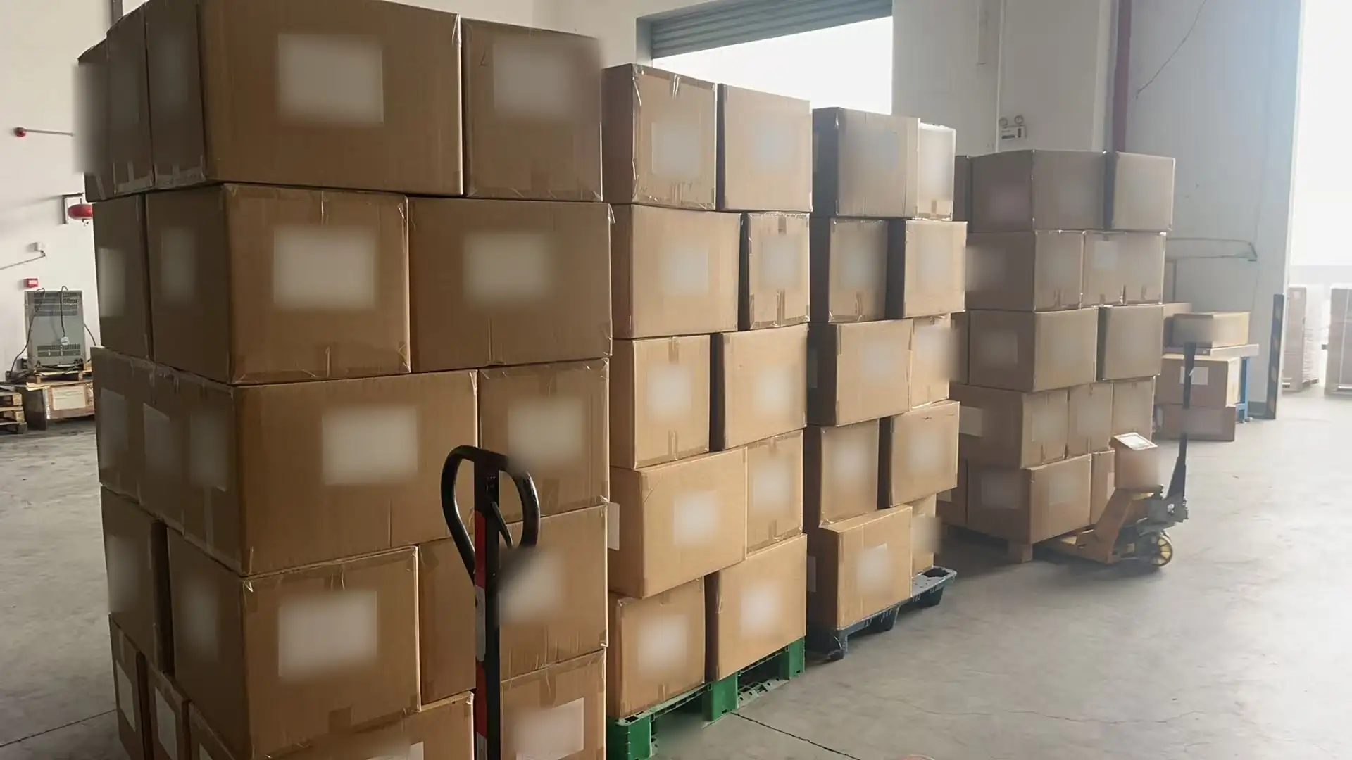 Original warehouse photograph of the packed project cartons, with label text locally softened for confidentiality